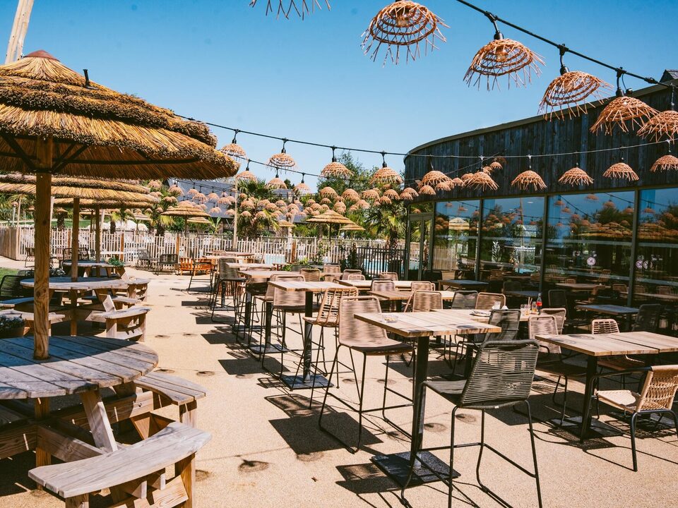 Het terras en zijn strooien parasols, bar-restaurant van Camping Portland